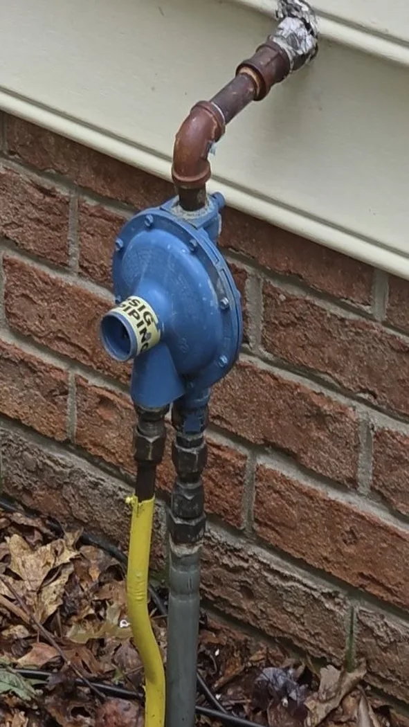 Old faded weathered propane regulator still mounted on the exterior wall before replacement